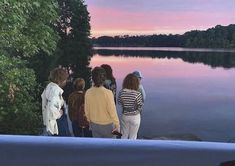 group of people standing at the edge of a body of water watching the sun set