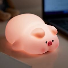 a small pink pig lamp sitting on top of a table next to a laptop computer