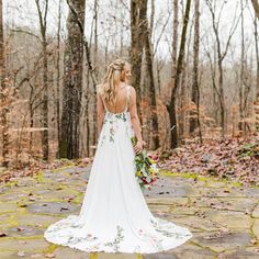 a woman in a wedding dress standing on a stone path with trees and leaves around her