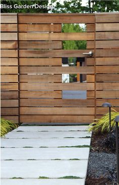 a wooden fence with grass growing on the ground and in front of it is a white walkway