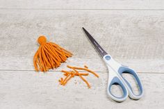 a pair of scissors and orange thread on a white wooden surface with an orange tassel