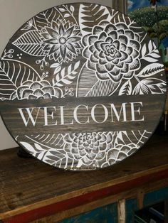 a welcome sign on top of a wooden table with flowers and leaves painted on it