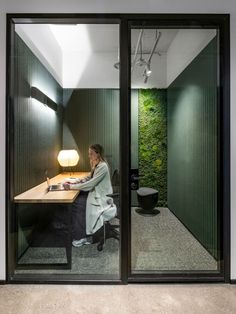 a woman sitting at a desk in front of a sliding glass door that leads to an office