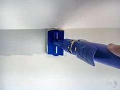 a person is using a blue tool to fix a wall with white paint on it