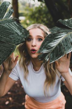 a woman holding two large green leaves in front of her face