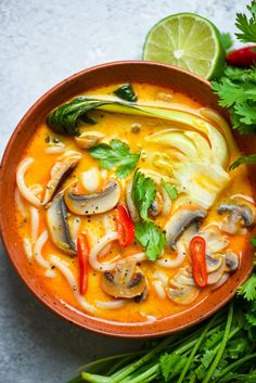 an overhead view of a bowl of soup with noodles, mushrooms and green vegetables on the side