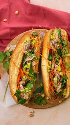 two sub sandwiches with meat, lettuce and carrots on a wooden platter