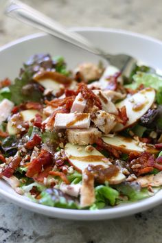 a salad with chicken, lettuce and bacon in a white bowl on a marble table