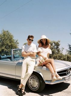 a man and woman sitting on the hood of a car with their arms around each other