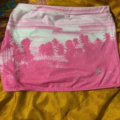 a pink and white shirt with palm trees on the front is laying on a yellow blanket