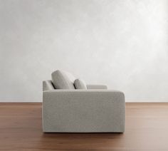 a couch sitting on top of a wooden floor next to a white wall with two pillows