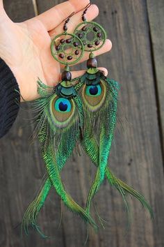 two peacock feathers are hanging from a person's hand with beaded earrings on them