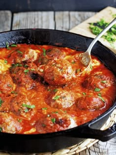 a skillet filled with meatballs and sauce on top of a wooden table next to bread