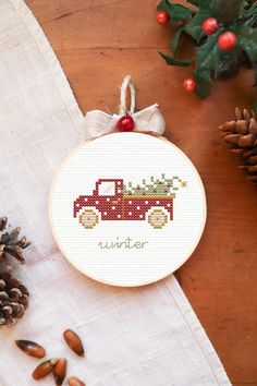 a cross stitch christmas ornament with a red truck on it and pine cones