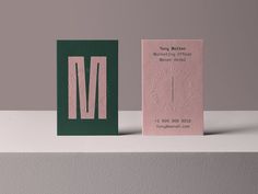 two business cards sitting on top of each other in front of a gray wall with the letter m