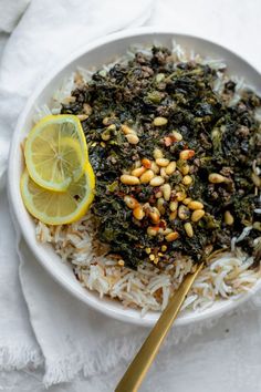 a white plate topped with rice and greens next to a lemon wedge on top of a towel