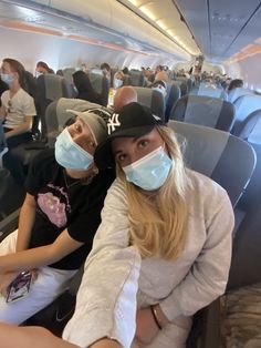 two people sitting on an airplane with masks covering their faces and looking at the camera