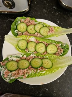 two lettuce wraps with cucumbers and tuna in them on a white plate