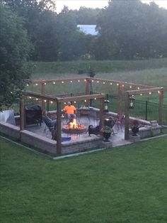 a backyard with a fire pit and string lights on the patio, surrounded by green grass