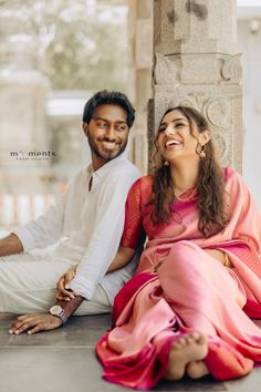 a man and woman sitting next to each other in front of a pillar smiling at the camera