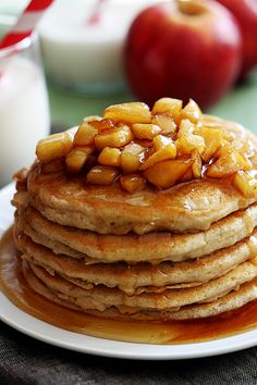 a stack of pancakes covered in syrup with apples next to milk and an apple on the side