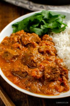 a white plate topped with rice and meat covered in sauce next to cilantro