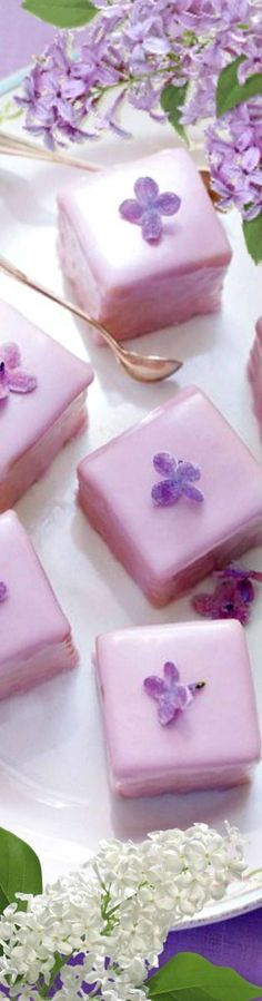 there are many small pieces of pink cake on the plate with purple flowers and greenery