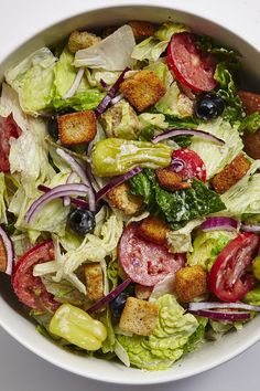 a salad with lettuce, tomatoes and croutons in a white bowl