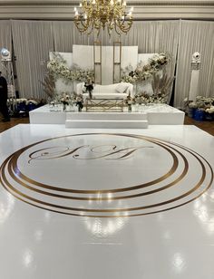 a white stage set up for a wedding ceremony with gold accents and chandelier