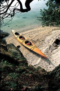 two canoes sitting on the shore of a lake near some rocks and trees with water in the background