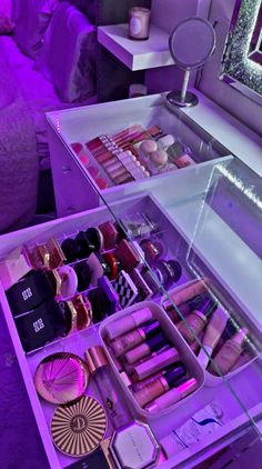 an assortment of makeup products displayed in a purple lit display case on a table next to a mirror