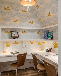 two wooden chairs sitting at a desk in front of a wall with birds on it