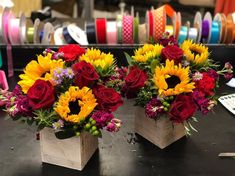 two wooden vases filled with colorful flowers on top of a black table next to some spools of thread