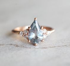 an engagement ring with two pear shaped blue topaztes and three diamonds on the side