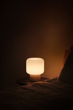 a white light sitting on top of a bed next to a night stand and pillow