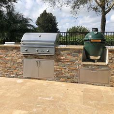 an outdoor bbq with grills and cabinets next to a fenced in area