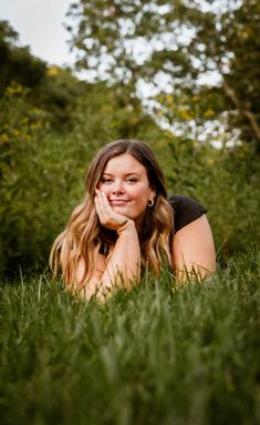 a woman laying in the grass with her hand on her chin and looking at the camera