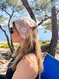 a woman wearing sunglasses and a crocheted hat looks out over the water from a beach