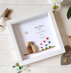 two pebbles sitting on a rock in a white shadow box next to flowers and seashells