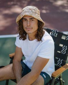 a man with long hair sitting in a chair wearing a hat and looking at the camera