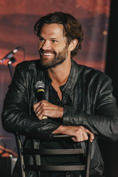 a man sitting in a chair with his arms crossed, smiling and holding a microphone