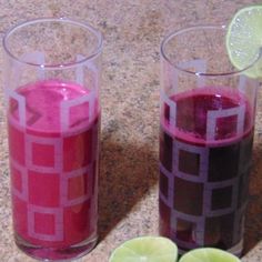 two glasses filled with liquid next to limes on a counter top and one has a slice of lime in it