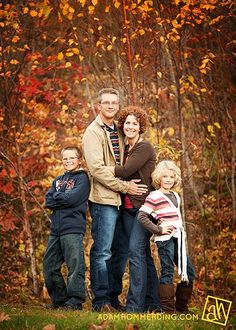 a family posing for a photo in front of some trees with fall leaves on it