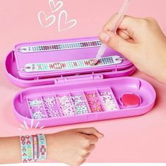 a person is holding a pencil and some beads in a pink case on a table