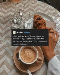 a cup of coffee sitting on top of a table next to a croissant