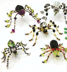 several spider brooches are arranged on a white surface with black, green, yellow and red beads