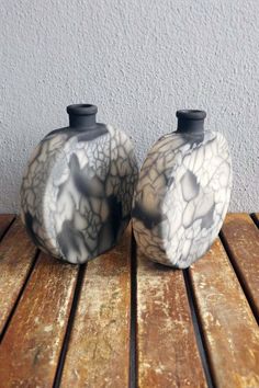 two black and white vases sitting on top of a wooden table next to each other