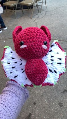 a red teddy bear sitting on top of a white and green object in someone's hand