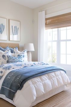 a bed with blue and white comforters in a bedroom next to a window that has two pictures on the wall