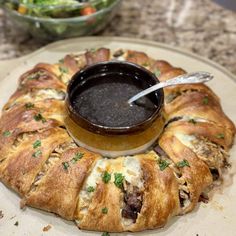 a croissant on a plate with a bowl of dipping sauce in the middle